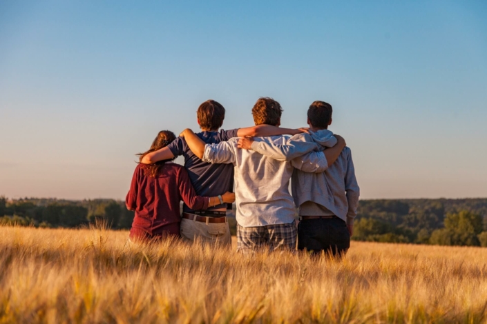 Vier junge Menschen stehen in einem Weizenfeld und schauen in die Ferne