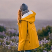 Eine junge Frau im gelben Regenmantel schaut auf ein Blumenfeld