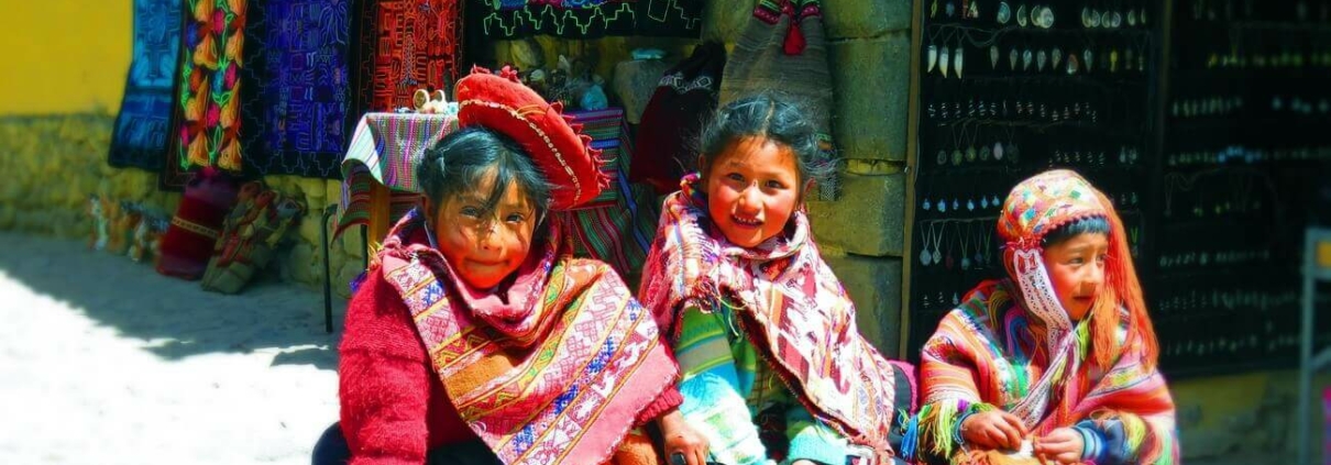 Drei Kinder aus dem Andenraum sind traditionell gekleidet und schauen in die Kamera.