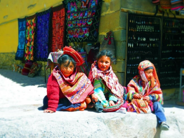 Drei Kinder aus dem Andenraum sind traditionell gekleidet und schauen in die Kamera.